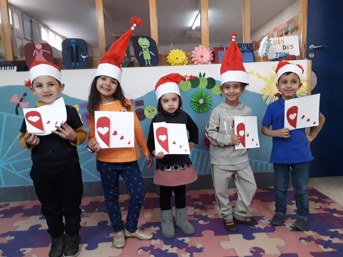 Cinq enfants de la maternelle des Iris, coiffés de bonnets rouges, présentent les cartes en forme de cœur qu’ils ont fabriquées en classe